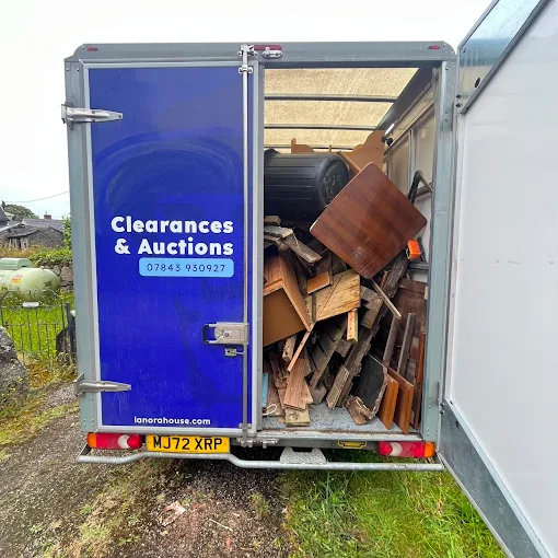 Rear of a blue Lanora House clearance van loaded with stacked wooden furniture and timber
