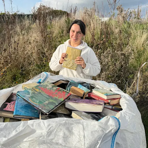 Member of the Lanora House team sorting a large pile of hardback and paperback books outdoors
