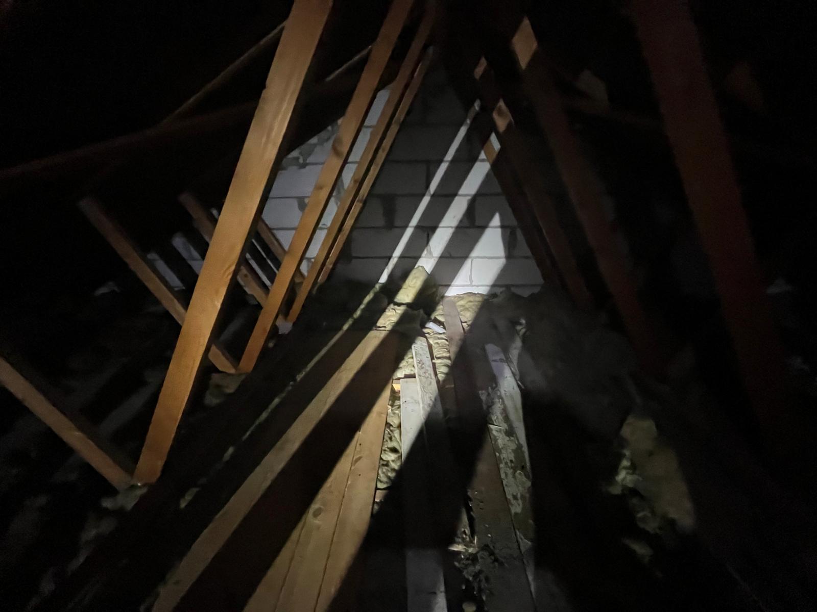 The same loft after clearance, empty down to bare joists and rafters with the gable wall visible