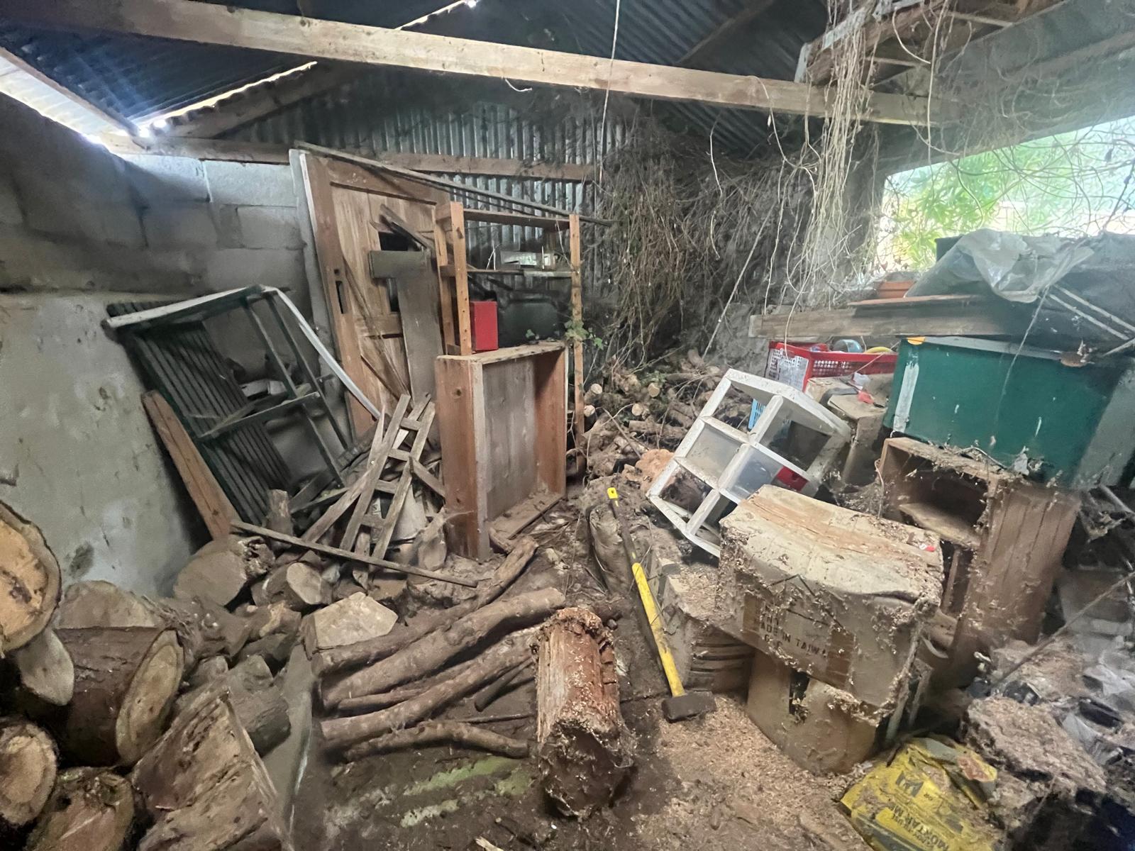 Collapsed store full of sawn logs, broken timber, an old window frame, sledgehammer and rusted metal frames