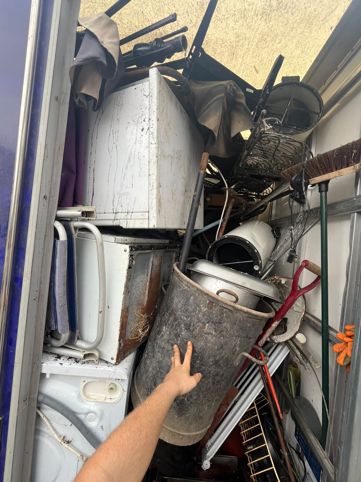 Loaded van interior with old appliances, a galvanised bin, garden tools and wire racking stacked to the roof